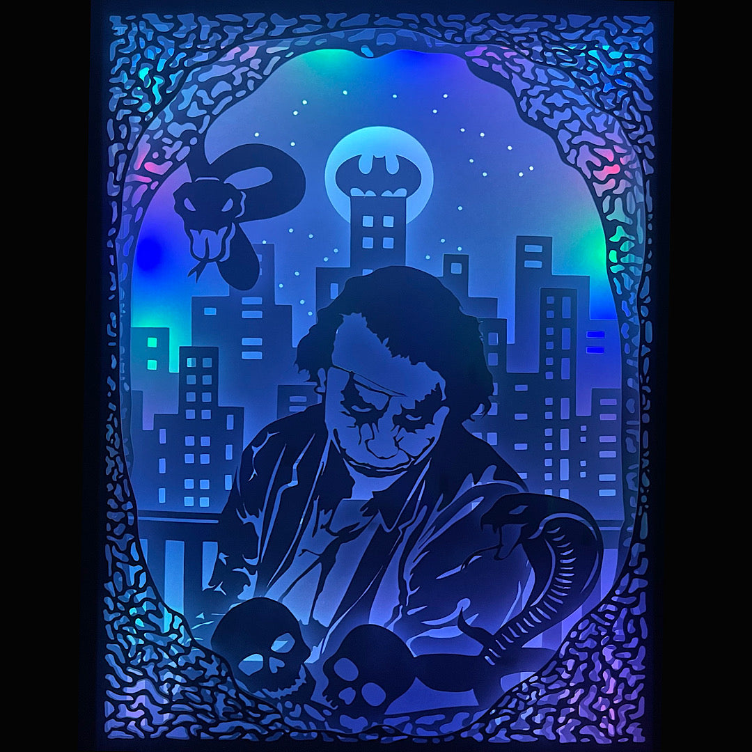 Joker, DC Comics, Gotham City, Batman, clown criminel, prince du crime, super-vilain, ennemi de Batman, Arkham, Harley Quinn, univers DC, comics cultes, maquillage Joker, sourire macabre, carte à jouer, Heath Ledger, Joaquin Phoenix, film Joker, Suicide Squad, personnage culte, tableau lumineux, lightbox, shadowbox, cadre lumineux, papier découpé, art lumineux, décoration murale, idée cadeau DC, déco geek, cadeau fan Batman