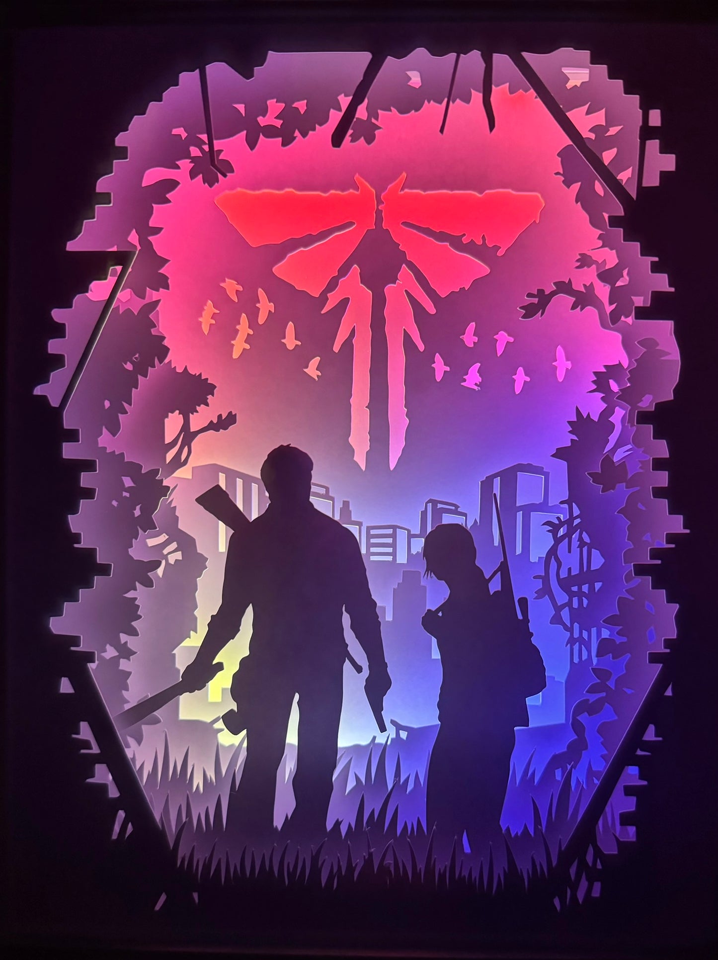 The Last of Us, TLOU, Naughty Dog, PlayStation, Joel, Ellie, Cordyceps, clickers, infectés, apocalypse, jeu vidéo culte, survival horror, aventure post-apocalyptique, monde détruit, relation père-fille, univers sombre, série HBO, Pedro Pascal, Bella Ramsey, combat pour survivre, route dangereuse, émotions fortes, tableau lumineux, lightbox, shadowbox, cadre lumineux, papier découpé, art lumineux, décoration murale, idée cadeau gamer, déco geek, cadeau fan The Last of Us
