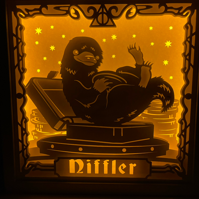 Niffleur, Nifler, Niffler Harry Potter, Les Animaux Fantastiques, Fantastic Beasts, J.K. Rowling, créature magique, voleur de trésors, poche ventrale, or et bijoux, Norbert Dragonneau, univers magique, saga Harry Potter, film Les Animaux Fantastiques, magie, créature attachante, monde des sorciers, personnage culte, tableau lumineux, lightbox, shadowbox, cadre lumineux, papier découpé, art lumineux, décoration murale, idée cadeau geek, déco magique, cadeau fan Harry Potter